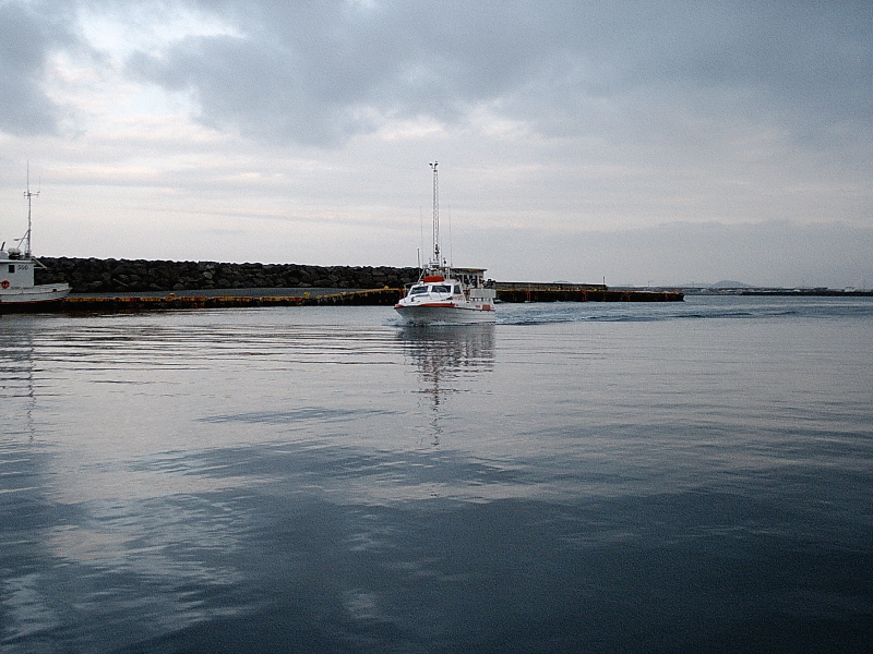 White cabin boat cruising in a harbor past a rock breakwater under gray clouds