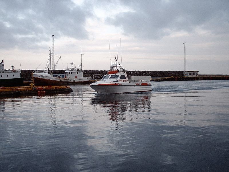 White and orange motorboat in a harbor near a fishing boat and breakwater
