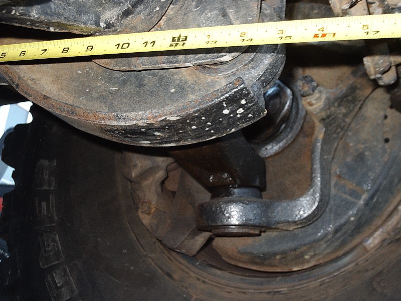 Rusty front axle differential and U-joint under a vehicle with a tape measure across the top.