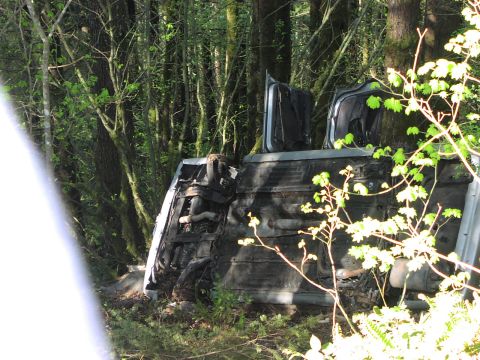 1993 Ford Bronco - Vehicle overturned in a forest setting, showing its undercarriage and open doors.