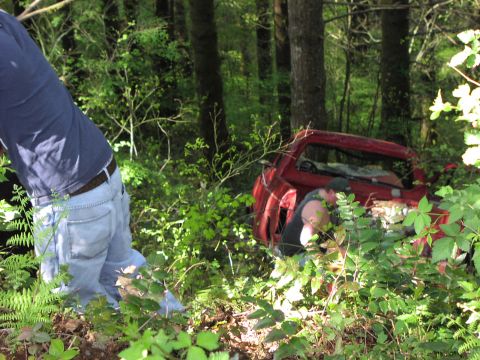 1993 Ford Bronco - Two people are working on a red pickup truck that is partially hidden by trees and foliage.