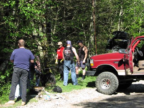 1993 Ford Bronco - Several people gather around a red off-road truck and a black SUV parked in a wooded area.