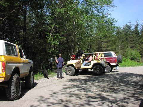 1993 Ford Bronco - Three off-road vehicles are parked on a dirt road surrounded by trees.