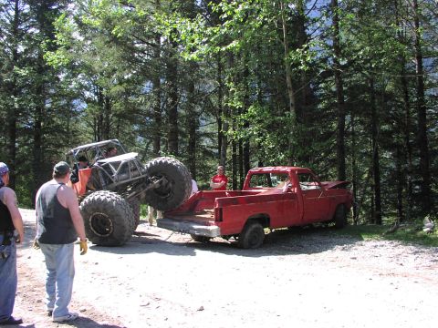 1993 Ford Bronco - An off-road vehicle is loaded onto the bed of a red pickup truck in a wooded area.