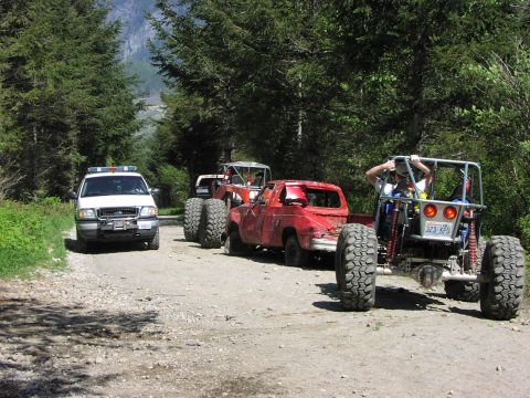 1993 Ford Bronco - Multiple off-road vehicles are parked on a dirt road surrounded by trees.