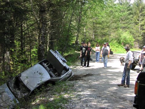 1993 Ford Bronco - A group of people observe a car that has gone off the road and overturned in the woods.