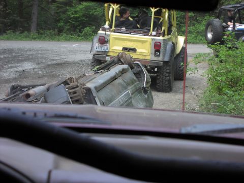 1993 Ford Bronco - A yellow Jeep Wrangler tows a heavily damaged vehicle on a gravel road, with another Jeep in the distance.