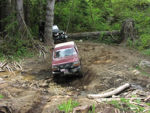 1993 Ford Bronco - A red SUV tackles a challenging off-road path, with another Jeep visible further up the trail.