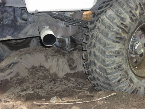 1993 Ford Bronco - The exhaust pipe and rear tire of an off-road vehicle are partially submerged in mud and dirt.