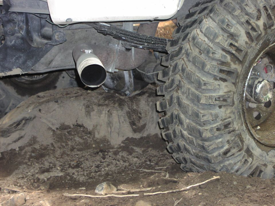 Close-up of a large off-road tire and exhaust pipe stuck in dirt