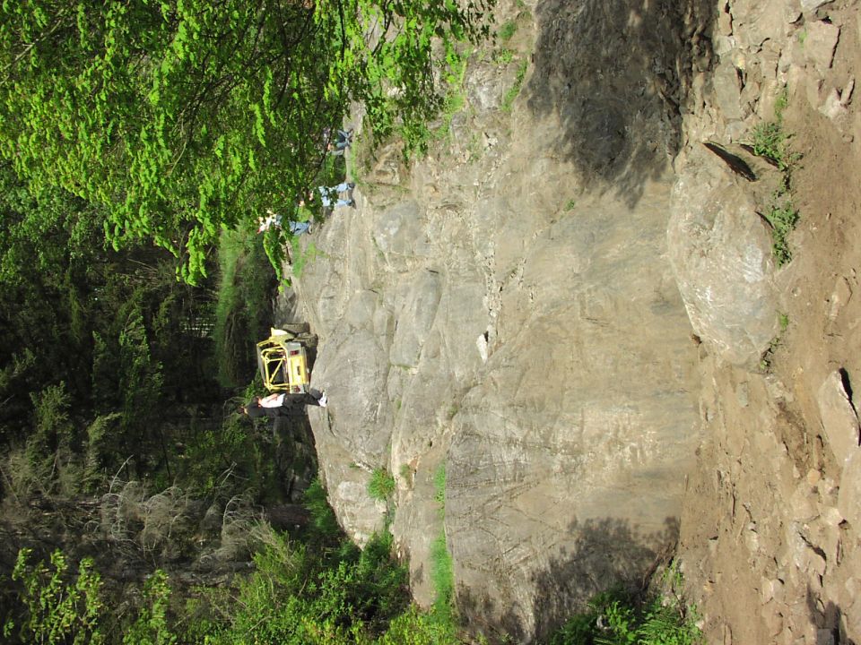 yellow off-road vehicle with roll cage on a steep, rocky incline near trees