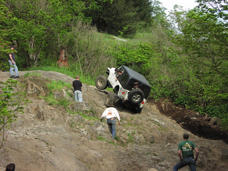 White Jeep Wrangler tilted on a rocky incline with a black soft top