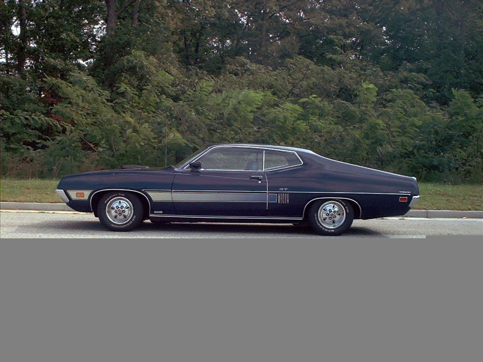 side view of a 1970 Ford Torino GT coupe parked on a road with trees in the background