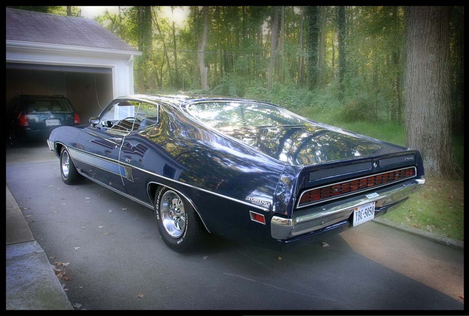 Dark blue 1970 Ford Torino GT parked in a driveway, rear 3/4 view. Chrome trim and wheels are visible