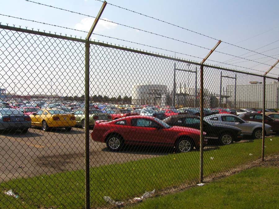 Cars parked in a lot behind a chain-link fence with barbed wire