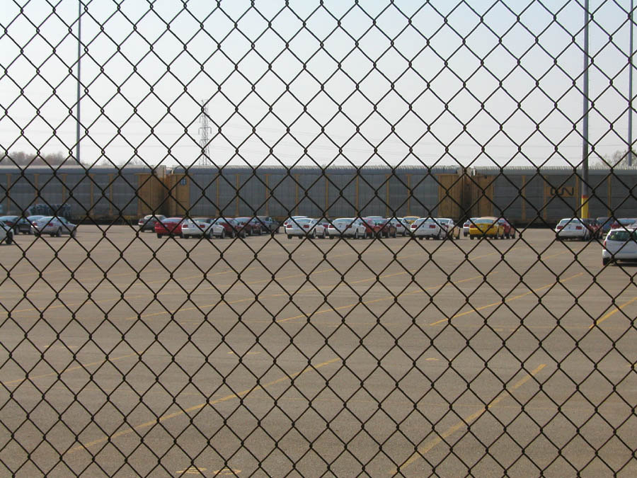 Parking lot with cars and train, seen through a chain-link fence