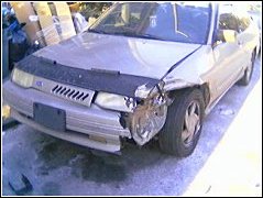 1991 Ford Escort - A sedan with heavy front-end damage sits parked, possibly awaiting repairs.