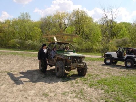 1992 Ford Bronco - A modified green off-road vehicle is parked on a dirt path, with a wooden rack secured to its roof.