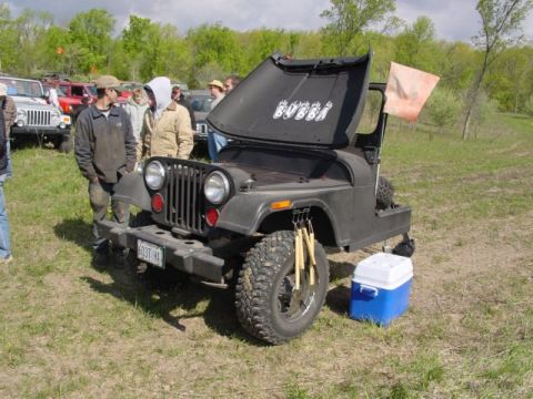 1992 Ford Bronco - A black Jeep CJ-7 with "Bubba" written on its open hood sits in a grassy field with people around it.