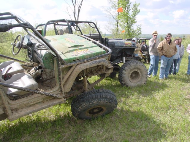 Muddy off-road vehicles parked on grass with people watching