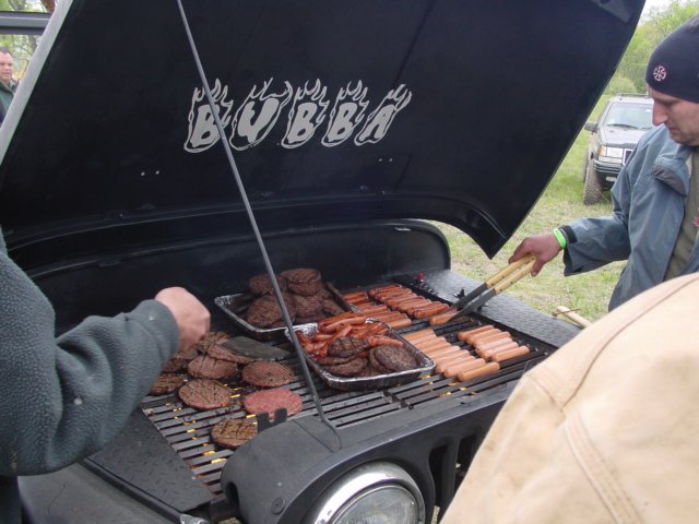 Jeep hood open, used as a grill for burgers and hot dogs. Text 'BUBBA' on hood. Another Jeep visible in background