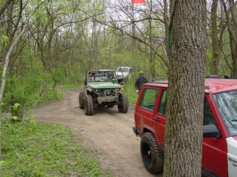 1992 Ford Bronco - Several off-road vehicles navigate a muddy trail through a dense forest.