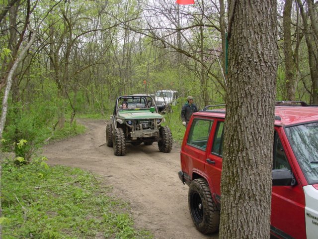 Red Jeep Cherokee and green off-road vehicle on a dirt path in a wooded area