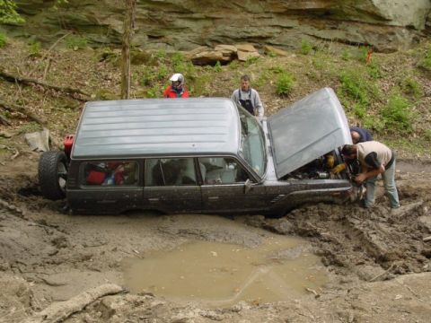 1992 Ford Bronco - Off-road vehicle stuck in mud, people attempting repairs.