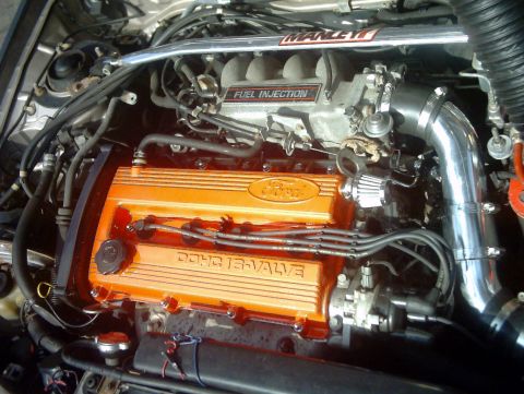 1991 Ford Escort - Close-up of a Ford engine orange valve covers and a chrome intake pipe.