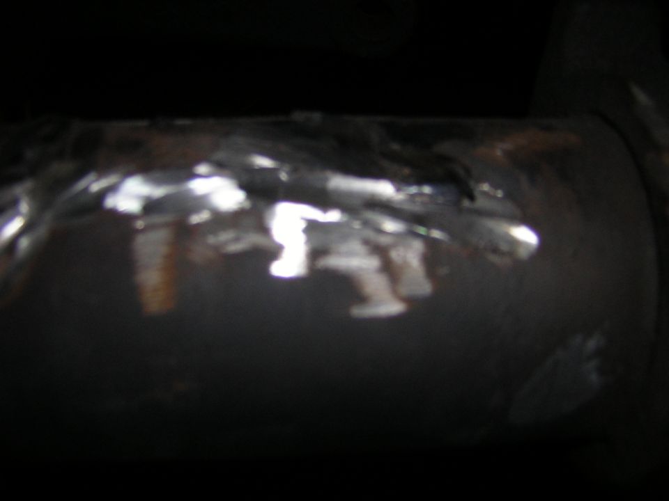 Ground-smooth weld beads on a rusty round steel axle tube under a truck