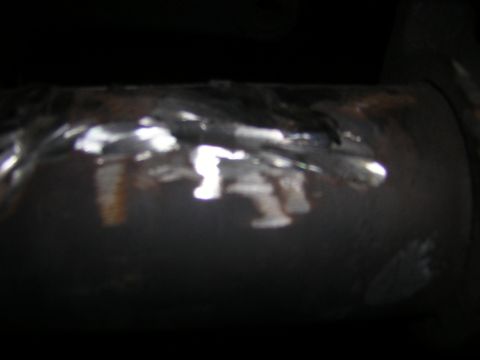 1995 Ford Bronco - Dim close-up of a cylindrical steel component, possibly a driveshaft or axle tube, with weld beads and rust marks along its reflective surf…