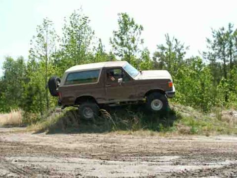 1988 Ford Bronco - This 1987 Ford Bronco is shown navigating an off-road trail with a wooded area behind it.