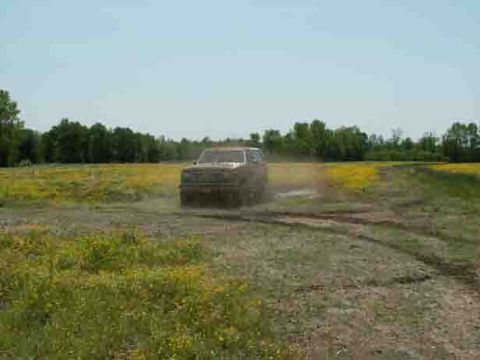 1988 Ford Bronco - A vehicle navigates a muddy track in a field under a clear blue sky.
