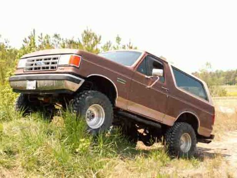 1988 Ford Bronco - Brown Ford Bronco with lifted suspension and off-road tires navigates a grassy incline.
