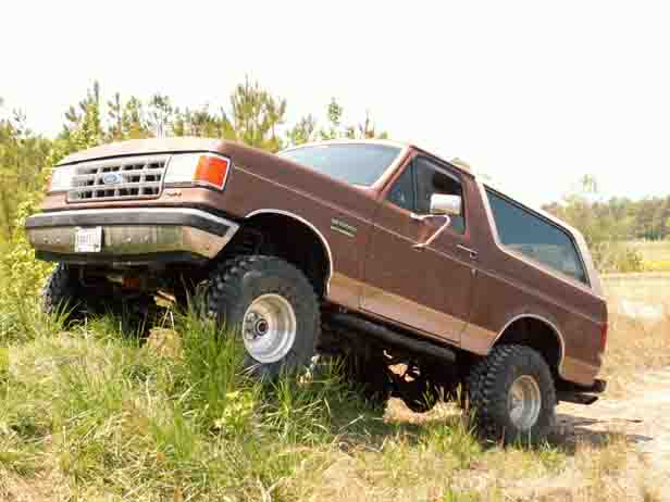 Brown Ford Bronco on grassy incline, lifted suspension, off-road tires, front grille visible