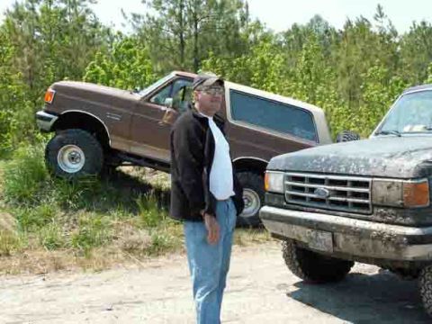 1988 Ford Bronco - A brown 1987 Ford Bronco is parked on a grassy incline next to a dark Ford F-Series truck.