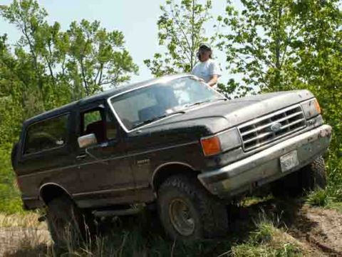 1988 Ford Bronco - This 1988 Ford Bronco is captured in a three-quarter front view while navigating a rough, wooded terrain.
