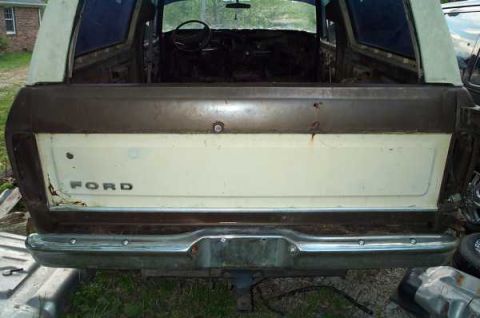 1979 Ford Bronco - The rear of a 1979 Ford Bronco is shown with its tailgate lowered, revealing the 'FORD' emblem on the cream-colored panel.