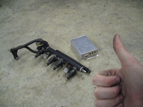 1987 Volkswagen Golf - A fuel rail assembly with injectors and a small electronic control unit are displayed on a concrete floor.