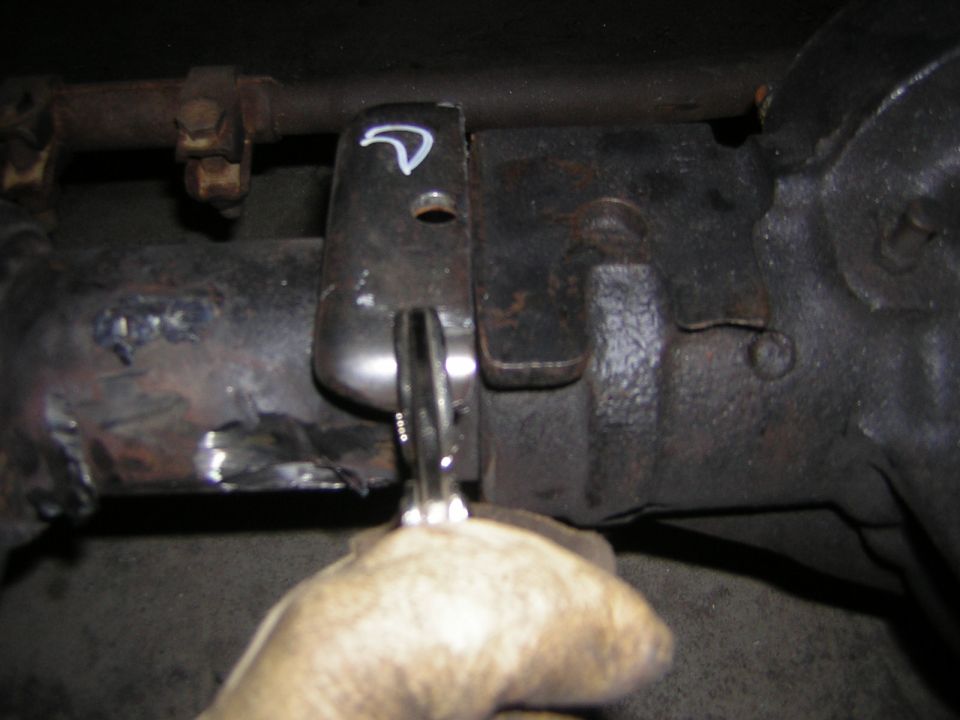 Hand using a ratchet on a rusty frame crossmember with a painted index mark