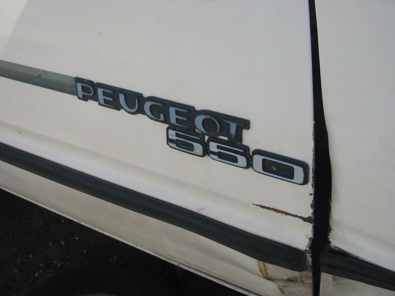 Chrome PEUGEOT 505 badge on a white car panel with rust at the seam