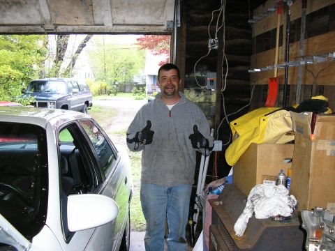 1998 Ford Taurus - A man stands in a garage, giving a thumbs-up, with a white car in the foreground and an SUV visible outside.