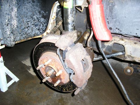 1998 Ford Taurus - Close-up of a 1998 Ford Taurus front brake assembly, showing wear and tear on the rotor and caliper.