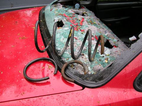 1998 Ford Taurus - Springs are resting on the hood of a red car with a broken rear window.