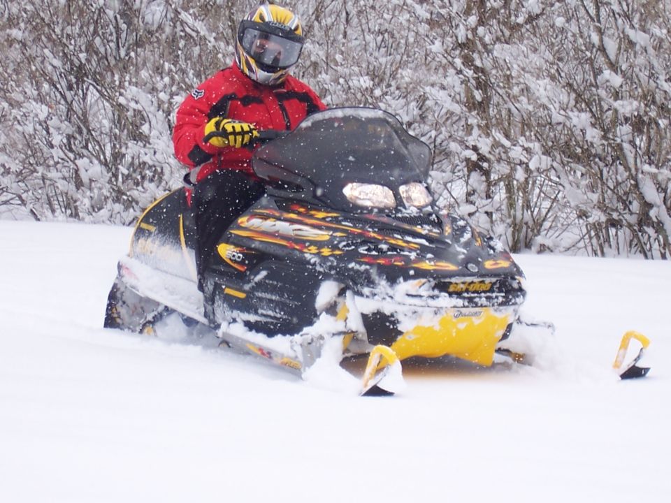 Rider in red jacket on black and yellow Ski-Doo snowmobile in deep snow