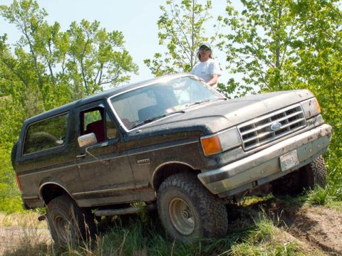 1988 Ford Bronco - A person stands behind a dark-colored Ford Bronco as it navigates an off-road incline.