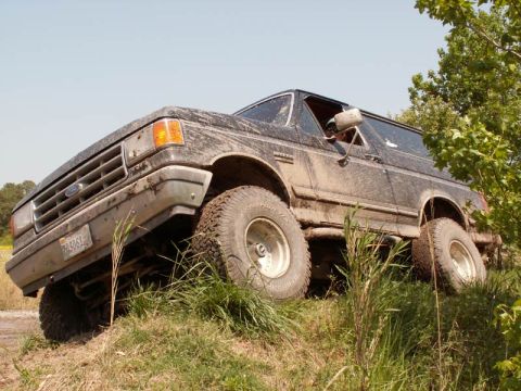 1988 Ford Bronco - This muddy 1987 Ford Bronco is shown from the front-right side as it navigates a grassy hill.