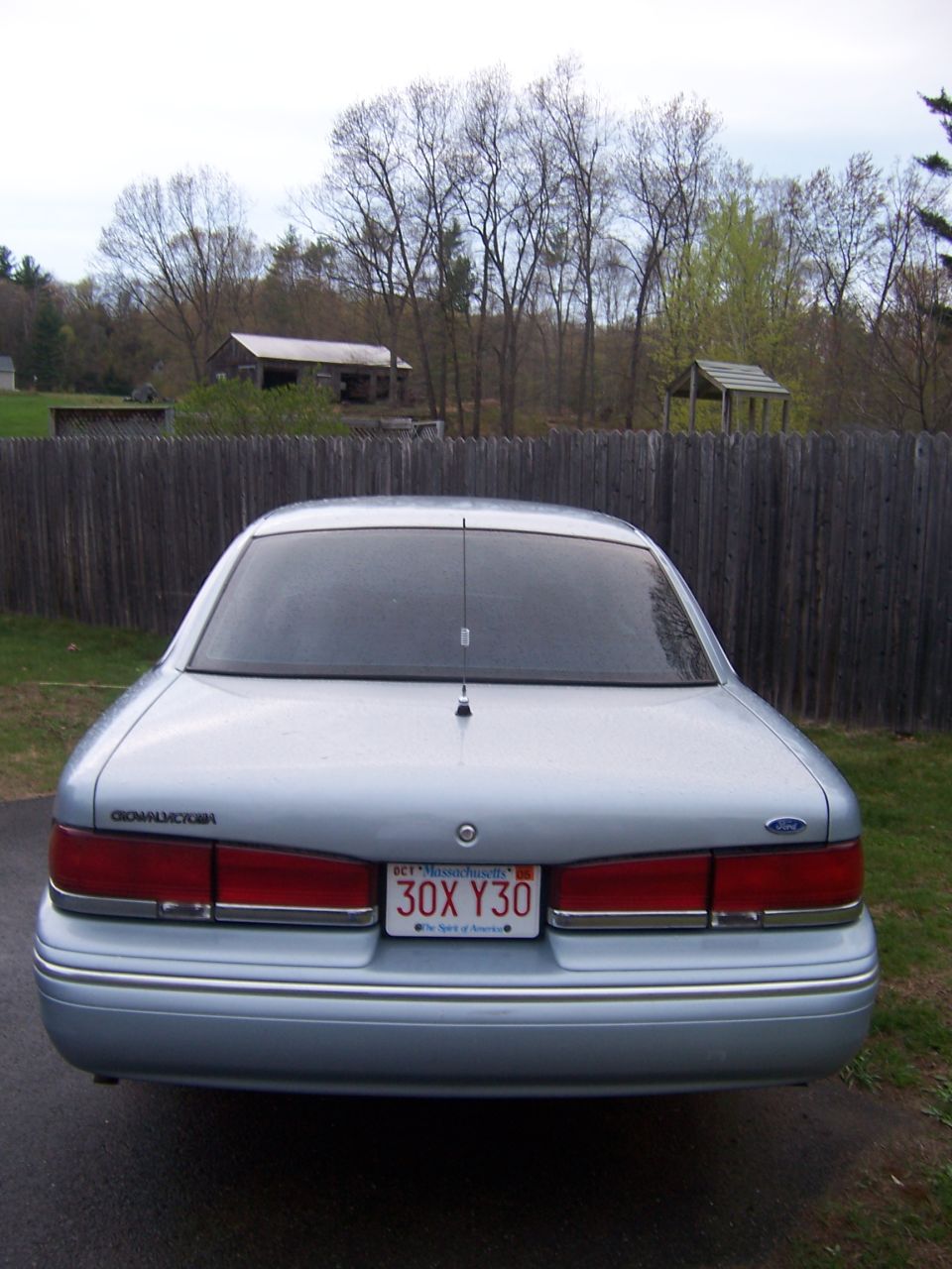 Rear view of a 1995 Ford Crown Victoria parked in front of a wooden fence and some buildings