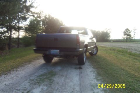 1995 Chevrolet Silverado 1500 - A dark-colored pickup truck is parked on a dirt road with trees in the background during the day.