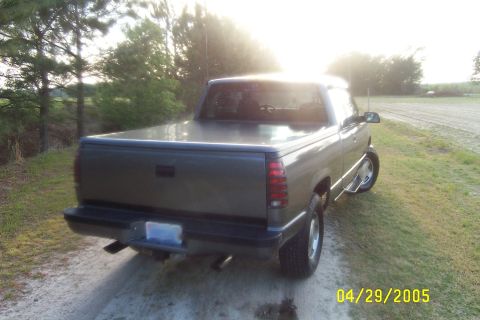 1995 Chevrolet Silverado 1500 - A gray Chevrolet C/K pickup truck is parked on a dirt road with trees in the background.